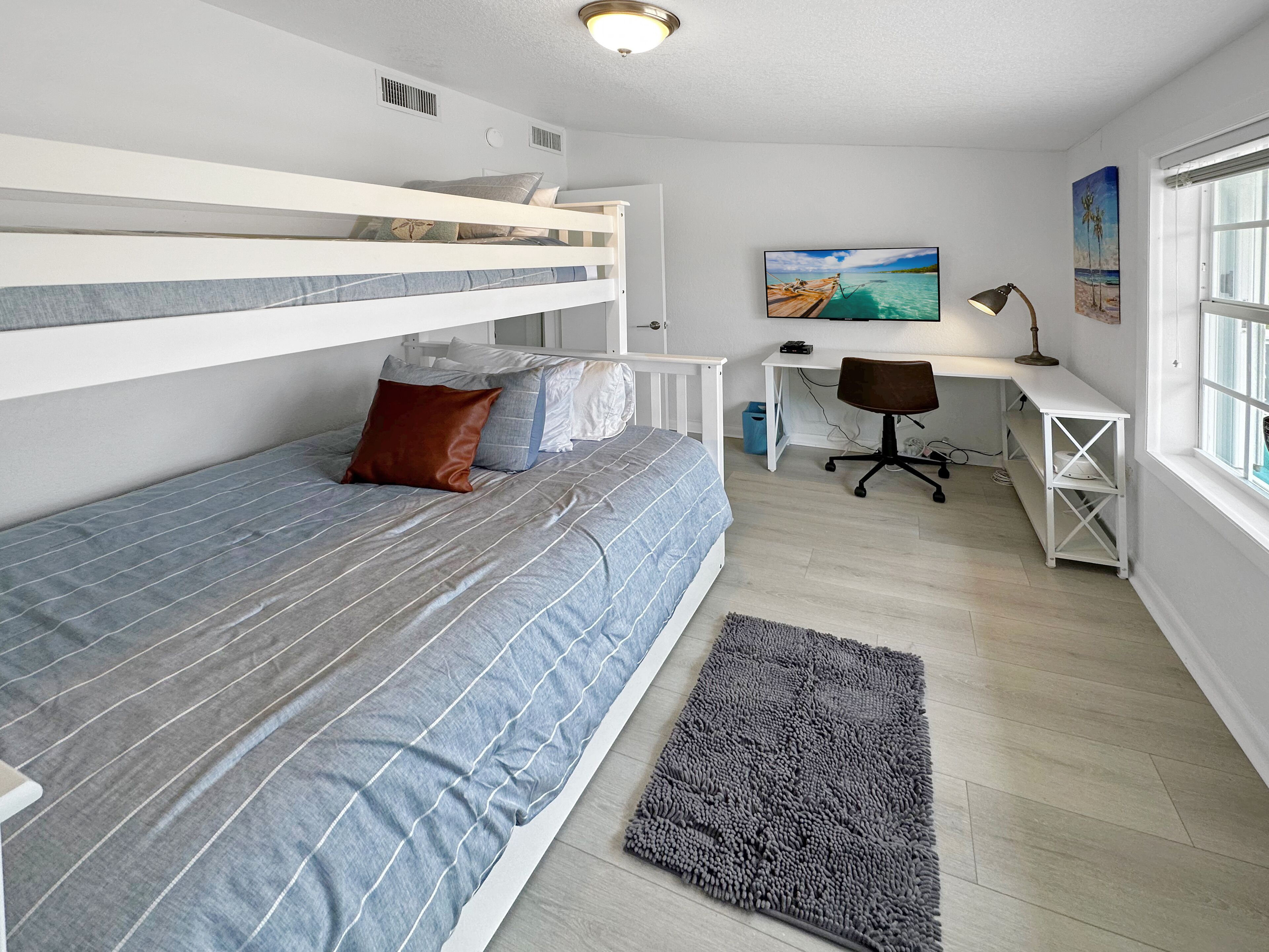 A bunk bed with a desk and chair, a painting, and a window.