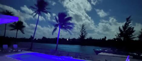 A poolside area with lounge chairs and a pool under a night sky with a visible moon.