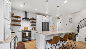 Une cuisine moderne avec des meubles blancs, un îlot central doté de tabourets de bar, un réfrigérateur en acier inoxydable et un four encastré.