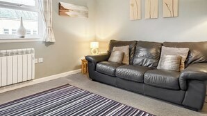 A living room with a leather sofa, a striped rug, a radiator, and wall art. - 2 bedroom accommodation in Bamburgh (Bamburgh)