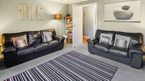 A living room with two black leather sofas, a striped rug, and a modern chandelier. - 2 bedroom accommodation in Bamburgh (Bamburgh)