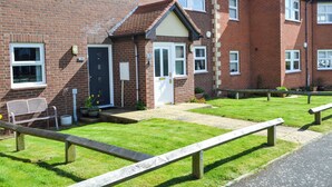 A brick residential building with a front garden, a bench, and a paved pathway. - 2 bedroom accommodation in Bamburgh (Bamburgh)