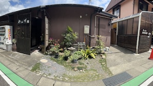 Ein Gebäude mit einem Getränkeautomaten, einem kleinen Garten mit Pflanzen und einem Schild auf Japanisch.