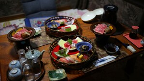 Ein Esstisch mit verschiedenen Speisen und Gewürzen, darunter Sushi und Sashimi, auf einer Tischmatte angerichtet.
