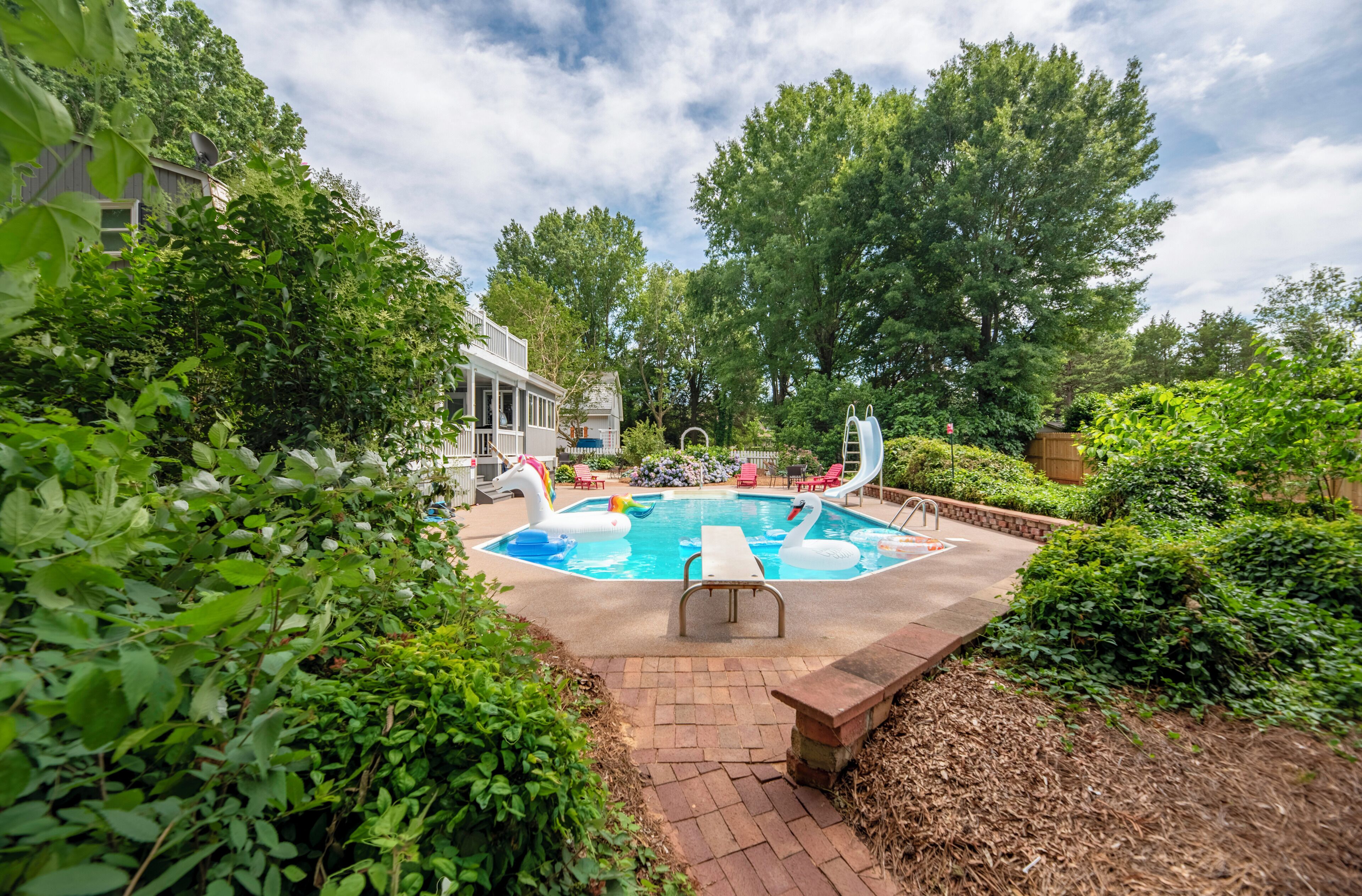 A backyard with a swimming pool, surrounded by lush greenery and a wooden deck.