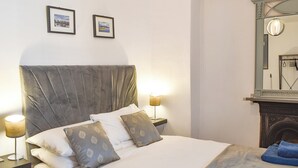 Ein ordentlich bezogenes Bett mit Kopfteil, zwei Nachttischlampen und einem Spiegel über dem Bett.
