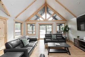 Un salon spacieux avec un plafond haut, des poutres en bois et de grandes fenêtres.
