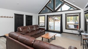 Un salón amplio con un sofá de cuero marrón, una mesa de centro de madera y ventanas grandes que ofrecen vistas al exterior.