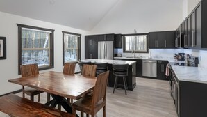 Una cocina moderna con armarios oscuros, electrodomésticos de acero inoxidable y una mesa de comedor de madera con sillas.