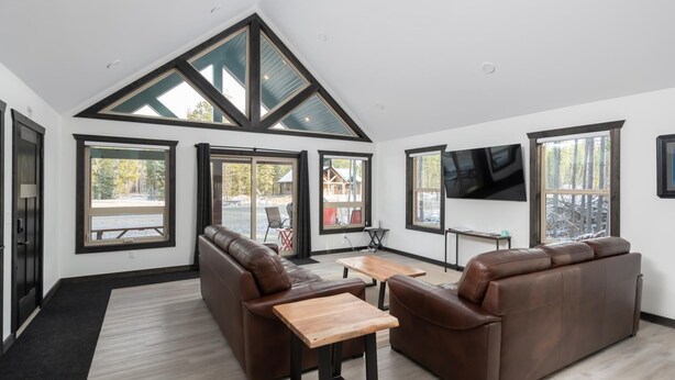 Una sala de estar moderna con techo alto, ventanas amplias, un sofá de cuero marrón, una mesa de centro de madera y un televisor de pantalla plana.