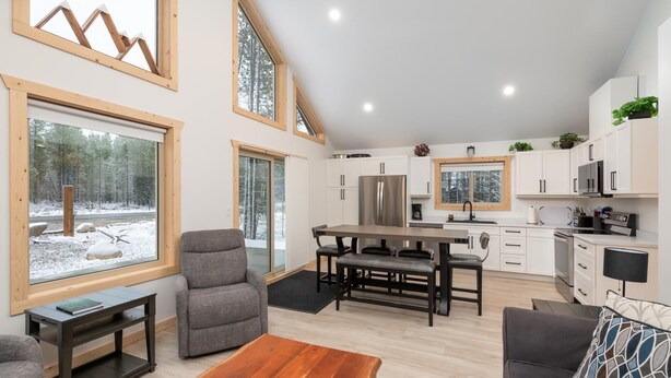 A modern kitchen with white cabinets, a stainless steel refrigerator, and a wooden dining table. - The Alpine Cabin Rental (British Columbia)