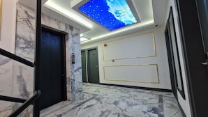 A hallway with marble flooring, a digital sky display, and a door with a red emergency light.
