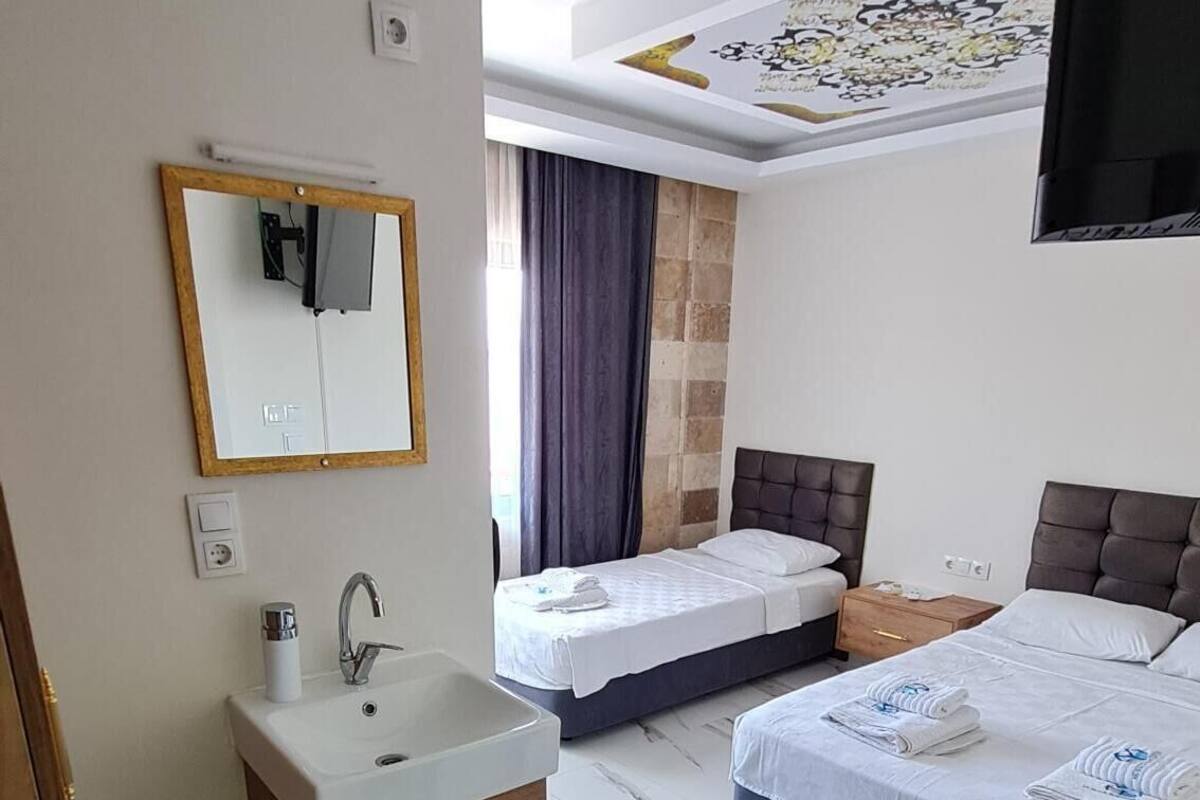 Habitación de hotel con un espejo grande, un lavamanos, dos camas, un televisor de pantalla plana y un techo con diseño decorativo.