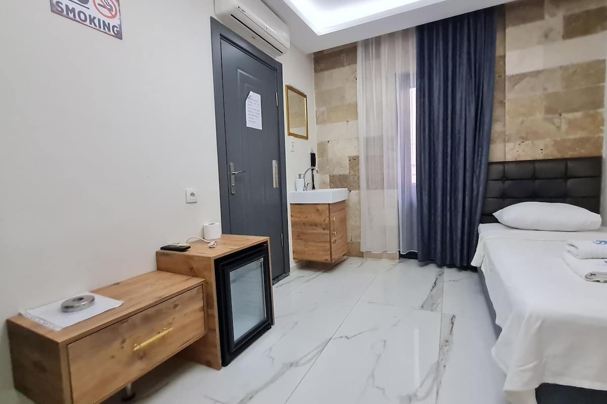 Una habitación de hotel con cama, escritorio, televisor pequeño, lavamanos y espejo.