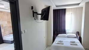 A modern hotel room with a bed, a flat-screen TV mounted on the wall, and a door leading to a balcony.
