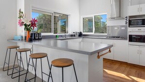 Een moderne keuken met een groot eiland, barkrukken en uitzicht op de buitenlucht.