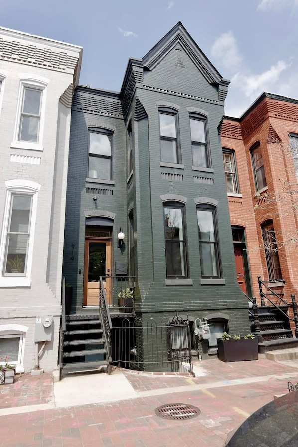 A row of three-story townhouses with a central entrance, a small porch, and a brick facade.