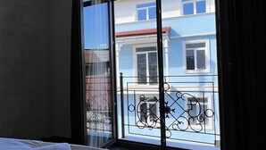 A hotel room with a large bed, a view of buildings through a window, and a patterned carpet. - Sota Metekhi Hotel (Tbilisi)