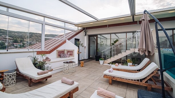 A rooftop terrace with lounge chairs, a staircase, and a glass-enclosed pool. - Sota Metekhi Hotel (Tbilisi)