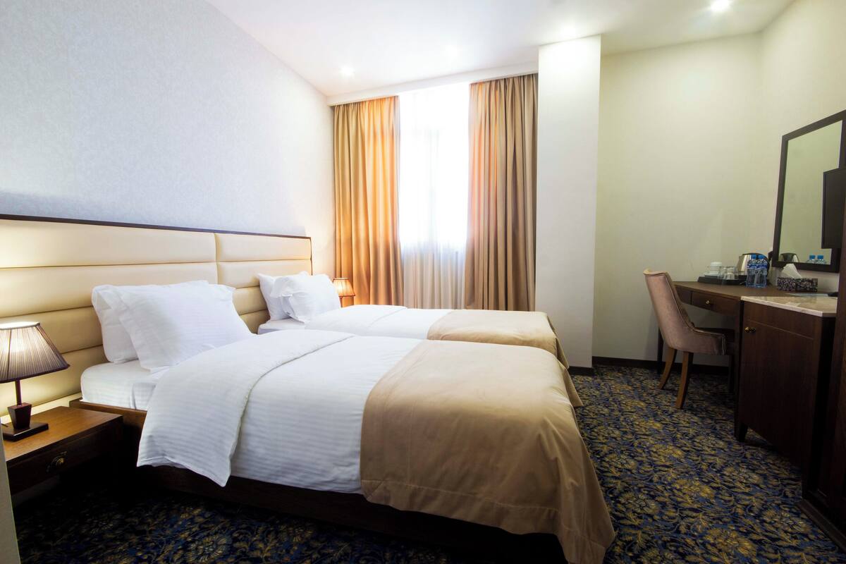 A hotel room with two beds, a desk, a chair, a lamp, and a large mirror.