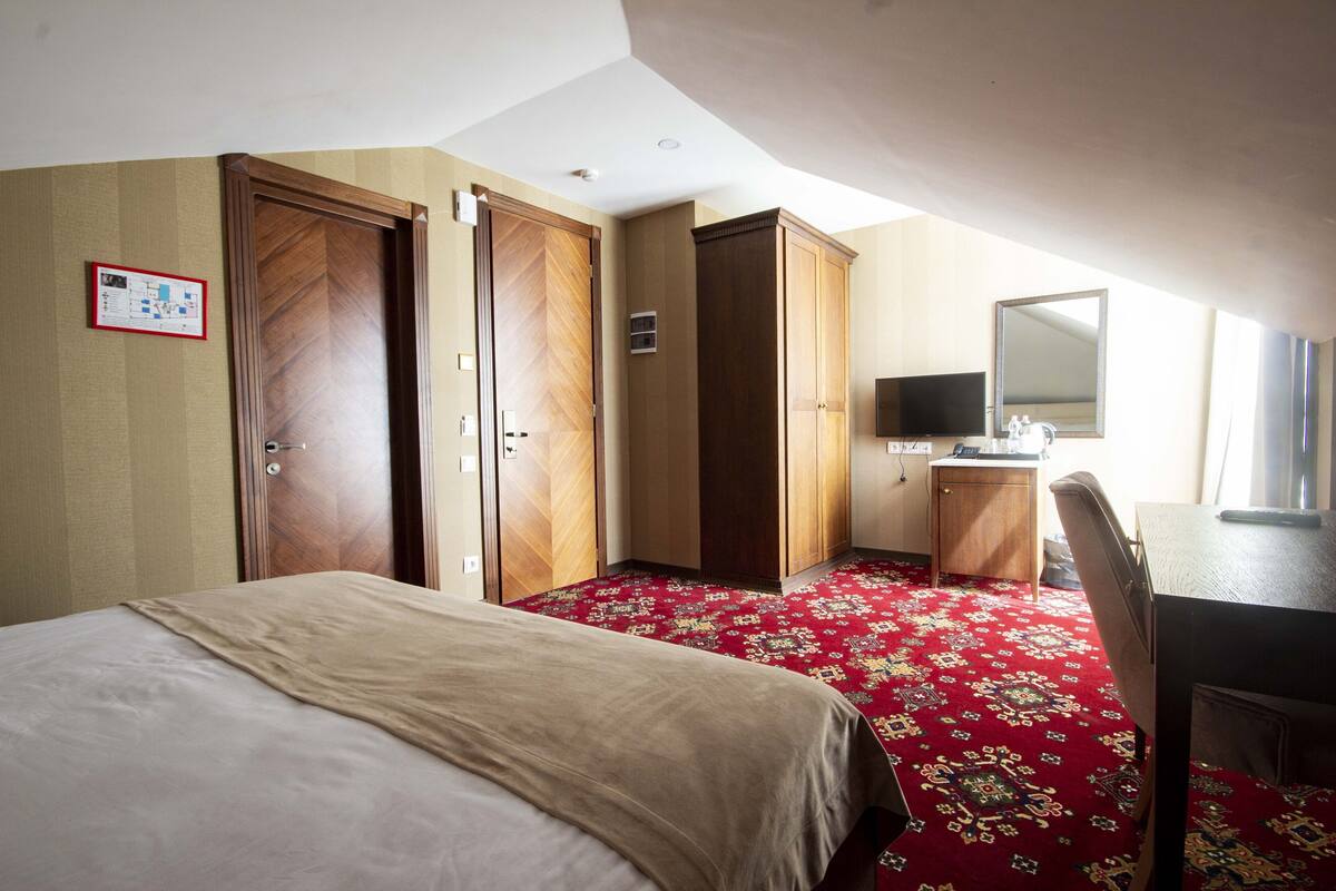 A hotel room with a bed, a desk, a chair, a television, and a wardrobe.