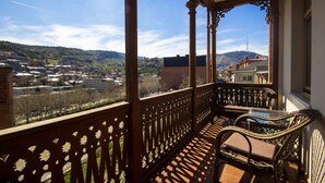 A balcony with a view of a town, wooden railings, and wicker furniture. - Sota Metekhi Hotel (Tbilisi)