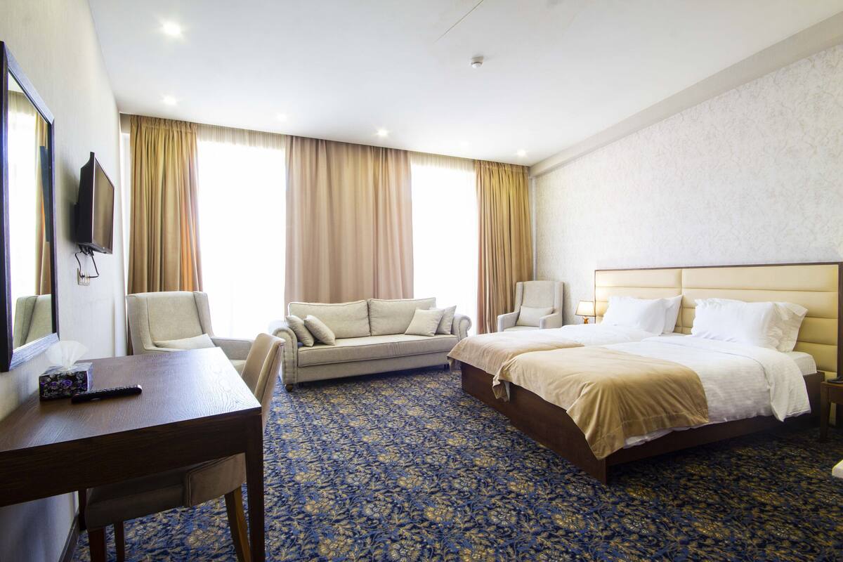 A hotel room with a bed, a sofa, a desk, and a TV.
