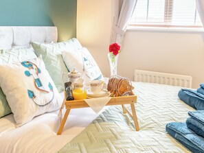 A neatly made bed with a tray of breakfast items, including toast, tea, and orange juice, in a room with a window and a radiator.
