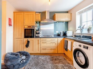 A modern kitchen with wooden cabinets, a built-in oven, a microwave, and a washing machine.
