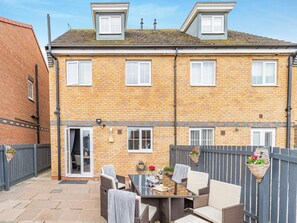 A two-story brick house with a patio area featuring wicker furniture and hanging flower baskets.