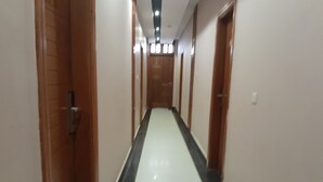 Um corredor comprido e estreito com portas de madeira em ambos os lados e chão branco.