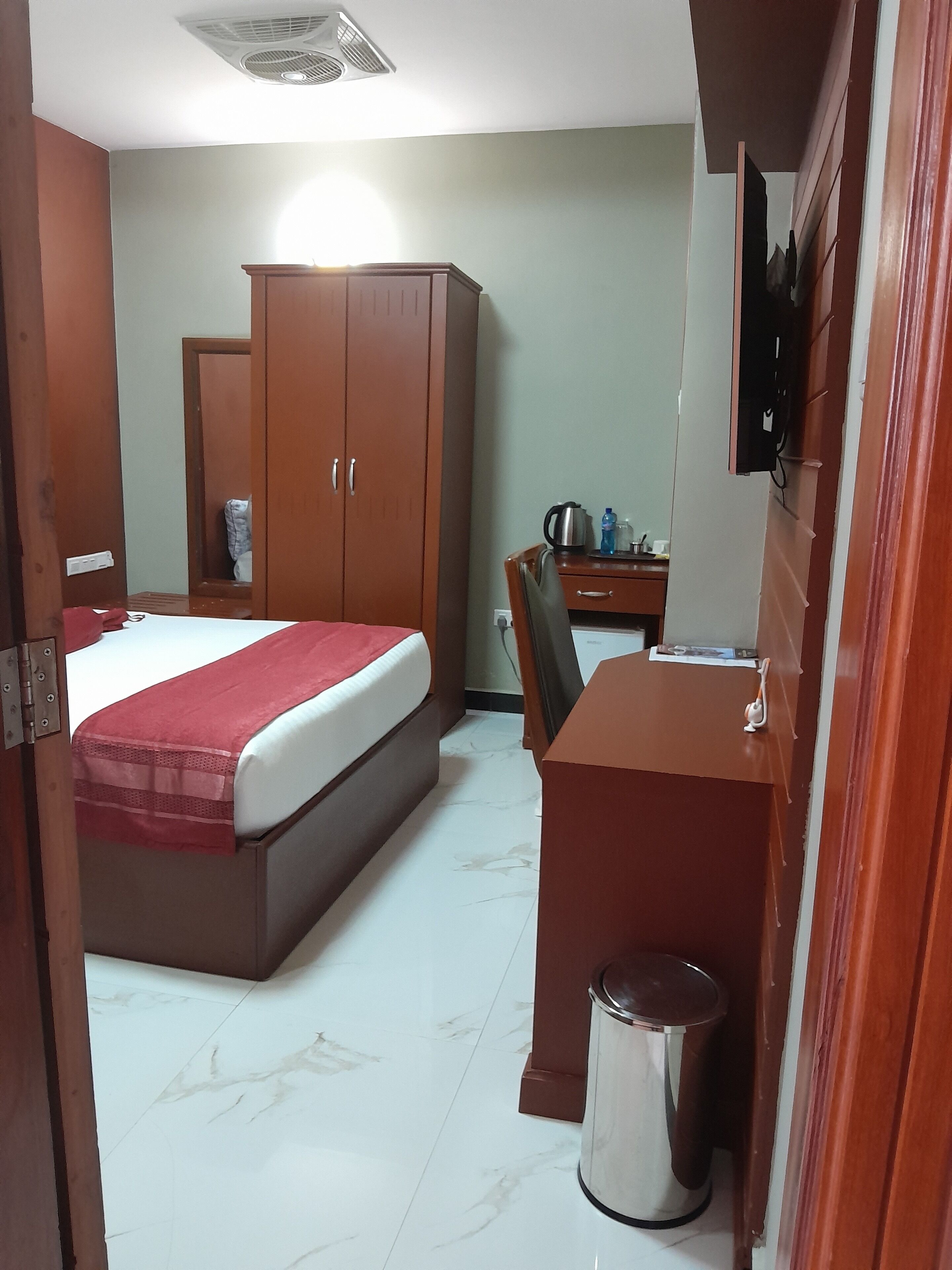 Una habitación de hotel con cama, escritorio, silla, armario y cubo de basura.
