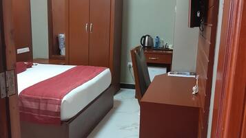 Una habitación de hotel con cama, escritorio, silla, armario y cubo de basura.