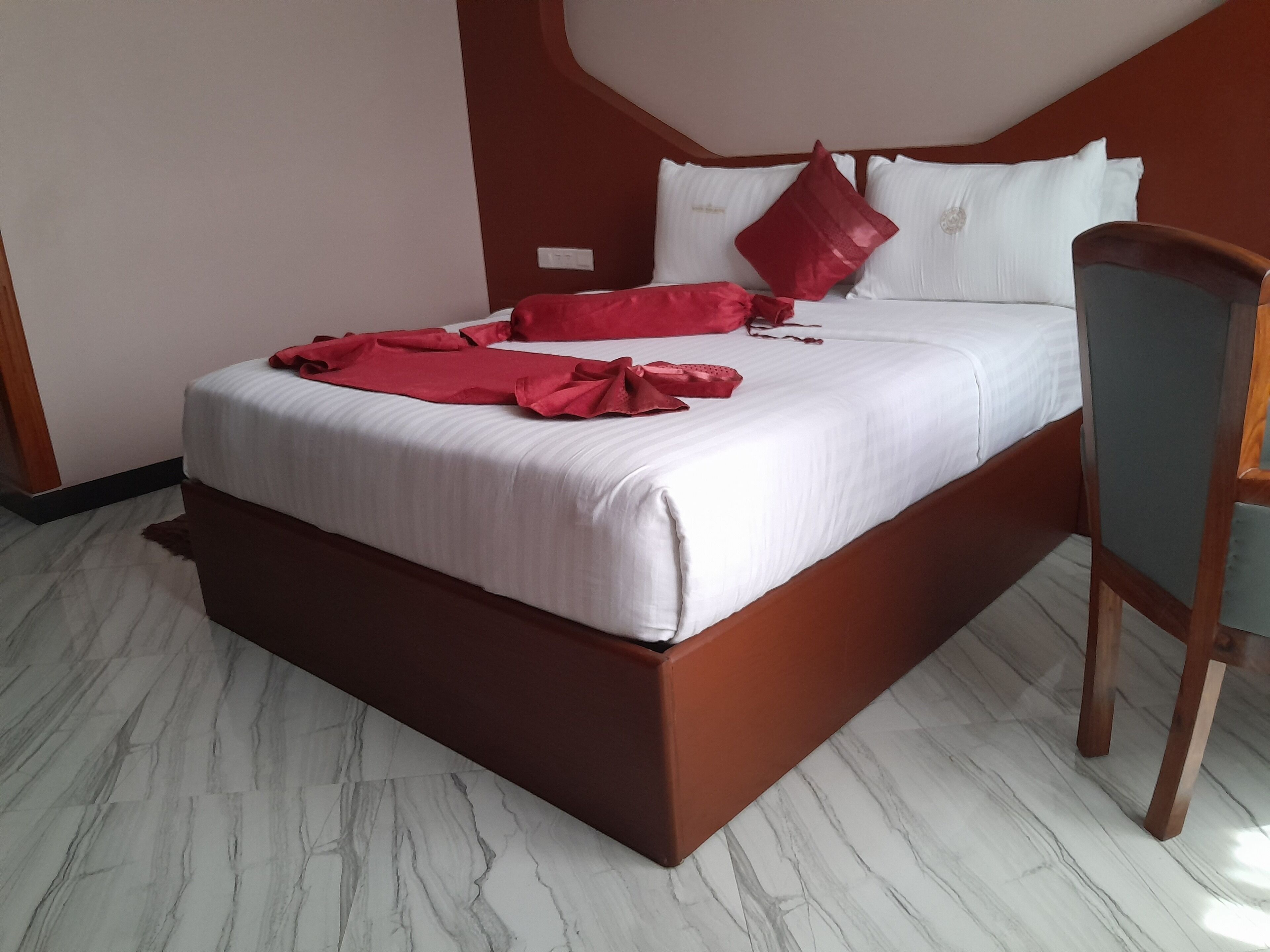 A bed with white bedding and red accents, a wooden headboard, and a chair with a wooden frame.