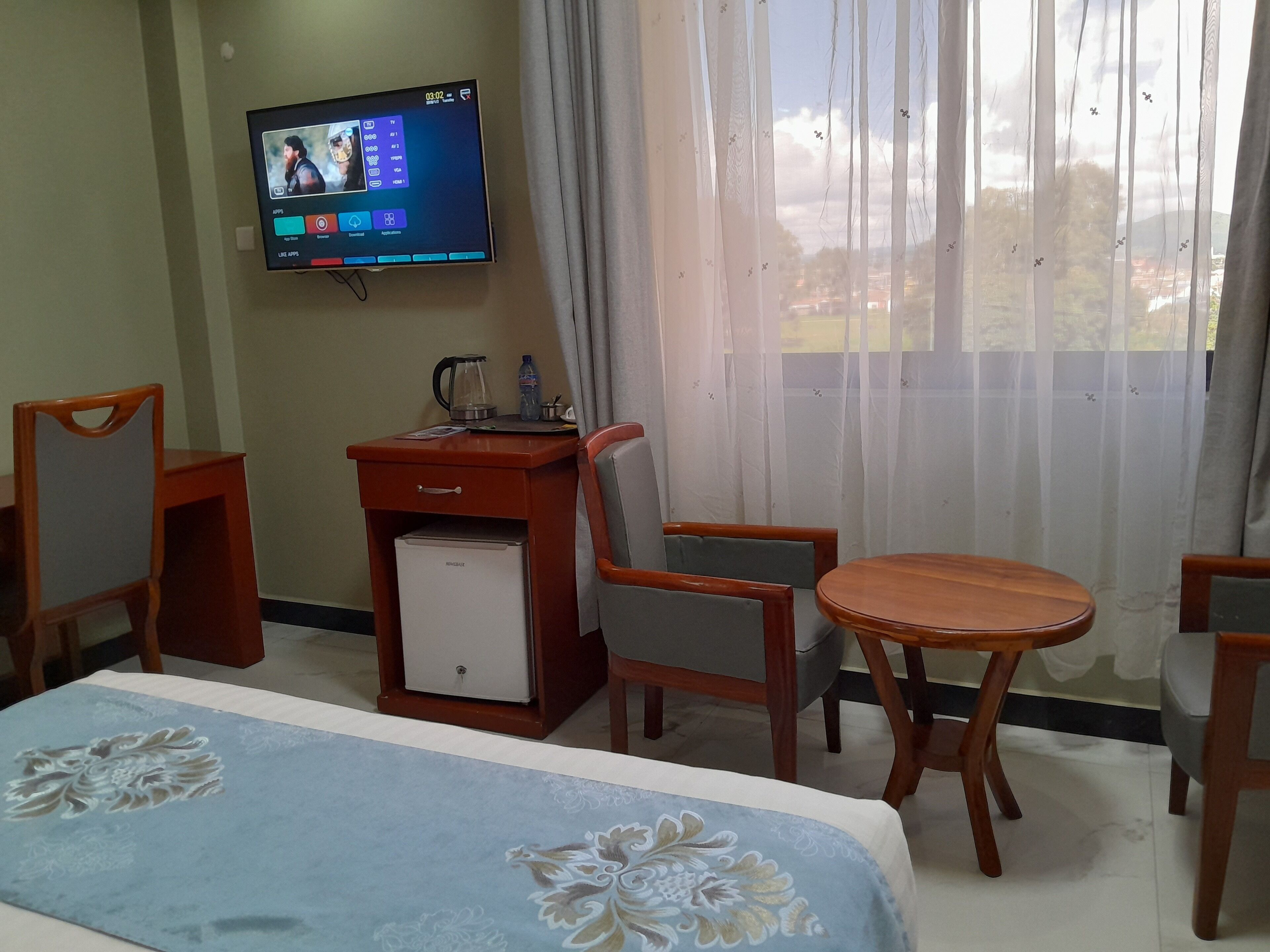 Une chambre d’hôtel comprenant un lit, un bureau avec un réfrigérateur, un téléviseur fixé au mur et une fenêtre avec des rideaux.