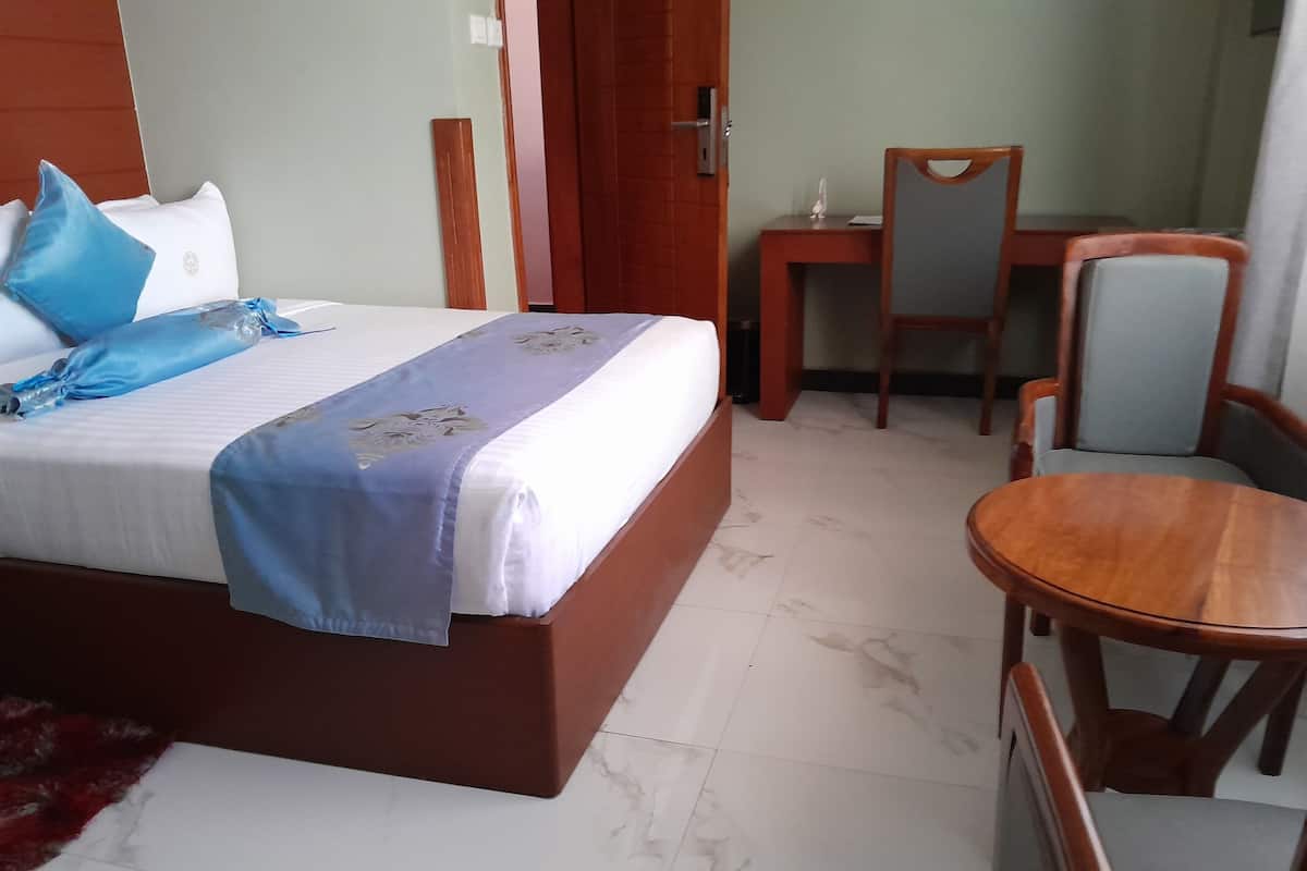 Una habitación de hotel con una cama, una silla de madera, una mesita y una puerta.