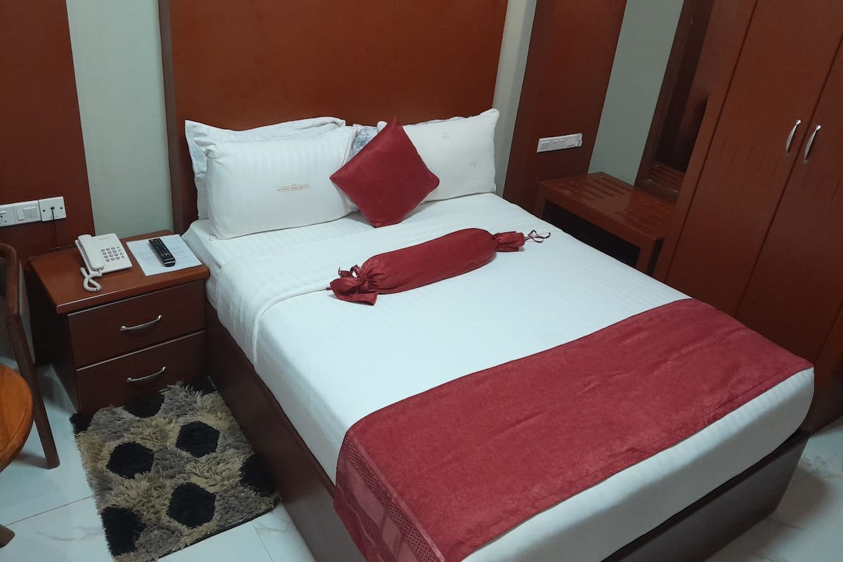 Una habitación de hotel con una cama, una mesita de noche con teléfono, un escritorio pequeño y un armario.