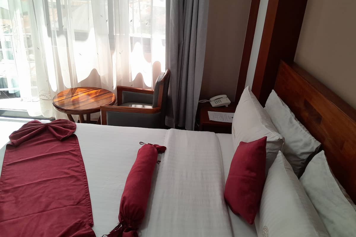 Una habitación de hotel con cama, una mesita de madera, una silla y una ventana con cortinas.