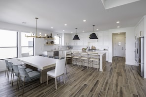 A modern kitchen with a central island, bar stools, pendant lighting, and a view to the outside. - New 5BR Sleeps 18 - Snow Canyon Views & Hot Tub (St. George)
