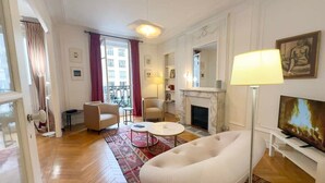 Ein geräumiges Wohnzimmer mit Kamin, Fernseher und einem großen Fenster mit Vorhängen.
