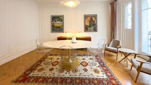 Ein Essbereich mit einem runden Tisch, klaren Stühlen, einem gemusterten Teppich und zwei gerahmten Bildern an der Wand.