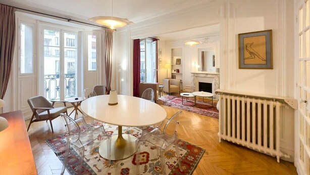 Ein geräumiges Wohnzimmer mit einem runden Tisch, klaren Stühlen, einem Kamin und großen Fenstern.