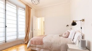Ein Schlafzimmer mit Bett, Nachttisch, Lampe und einem Fenster mit Vorhängen.