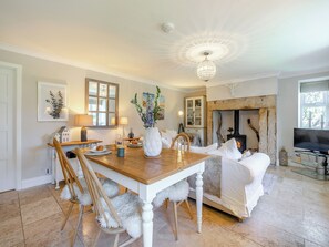A cozy living room with a wooden dining table, white upholstered furniture, a fireplace, and a television.