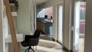 A modern interior with a herringbone floor, a black office chair, a wooden ladder, and a view into a kitchen area through a glass door.