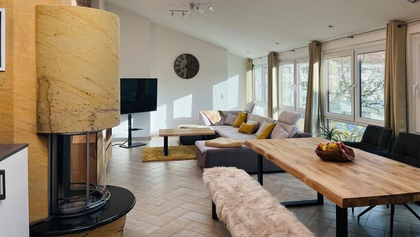 A modern living room with a large window, a wooden dining table, a sofa, and a TV.