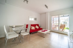 A modern living room with a glass dining table, white chairs, a red sofa, and a large sliding glass door leading to an outdoor area. - Two bedroom  in Spain, La Torre Golf Resort (Torre-Pacheco)