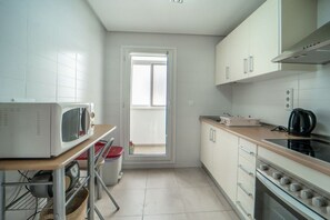 A compact kitchen with white cabinets, a microwave, a stove, and a window. - Two bedroom  in Spain, La Torre Golf Resort (Torre-Pacheco)