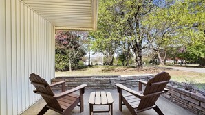 Une terrasse couverte, agrémentée de fauteuils Adirondack et d’une petite table, donnant sur un jardin aménagé et des arbres.