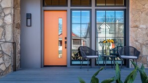 Une façade moderne agrémentée d’un mur en pierre, d’une terrasse en bois et d’une porte vitrée donnant sur un patio aménagé avec du mobilier d’extérieur et un vase rempli de tournesols.